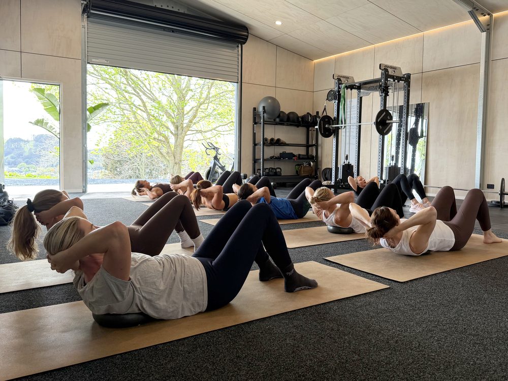 A Pilates class doing crunches, with the roller door open to the trees
